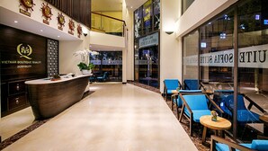 Un vestíbulo de hotel con mostrador de recepción, zona de estar y una escalera que conduce a un nivel superior.