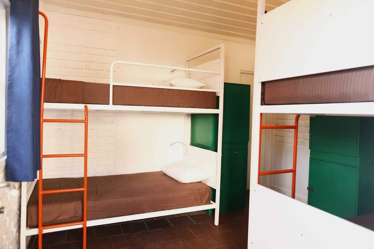 A bunk bed room with a white brick wall, green door, and orange metal ladder.