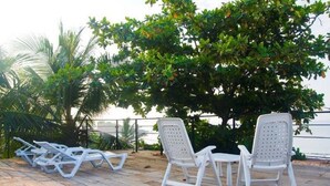 A deck with white lounge chairs and a small table, surrounded by lush greenery and overlooking a body of water. - Hangover Hostels at Mirissa (Mirissa)