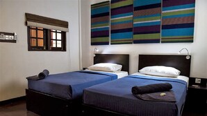 A hotel room with two beds, a window with a blind, a wall-mounted air conditioning unit, and a set of colorful striped artworks. - Hangover Hostels at Mirissa (Mirissa)