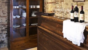 A rustic room with exposed brick walls, a wooden cabinet with glass doors, and a bar area with wine bottles and glasses.
