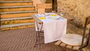 An outdoor dining area with a table set for two, a chair, and a wooden bench.