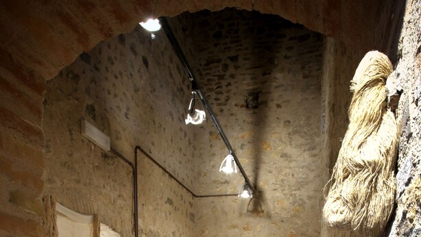 A narrow, stone-walled corridor with tables and chairs set up for dining, suggesting a restaurant or dining area within a historic building.