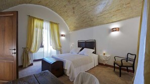 A bedroom with a wooden ceiling, a bed with white bedding, a nightstand with a candle, and a chair.