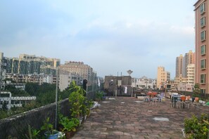 Una terraza en la azotea con plantas en macetas, una pequeña construcción y vistas de la ciudad.