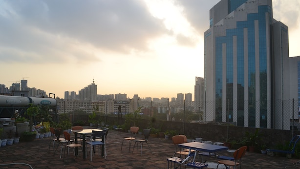 A rooftop terrace with tables and chairs, overlooking a cityscape with modern buildings.