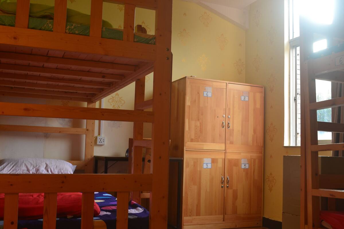 A bunk bed room with a wooden wardrobe and a window.