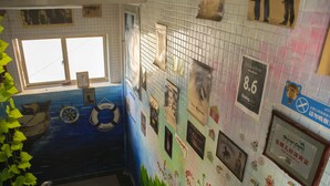 A tiled wall with various framed pictures and awards, a window, and a plant.