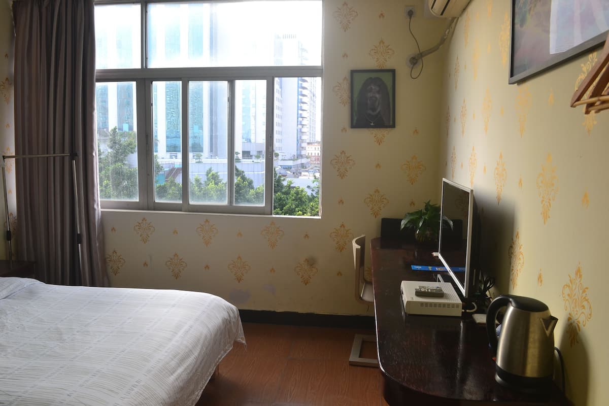 A hotel room with a bed, a desk with a laptop, a kettle, and a window with a city view.