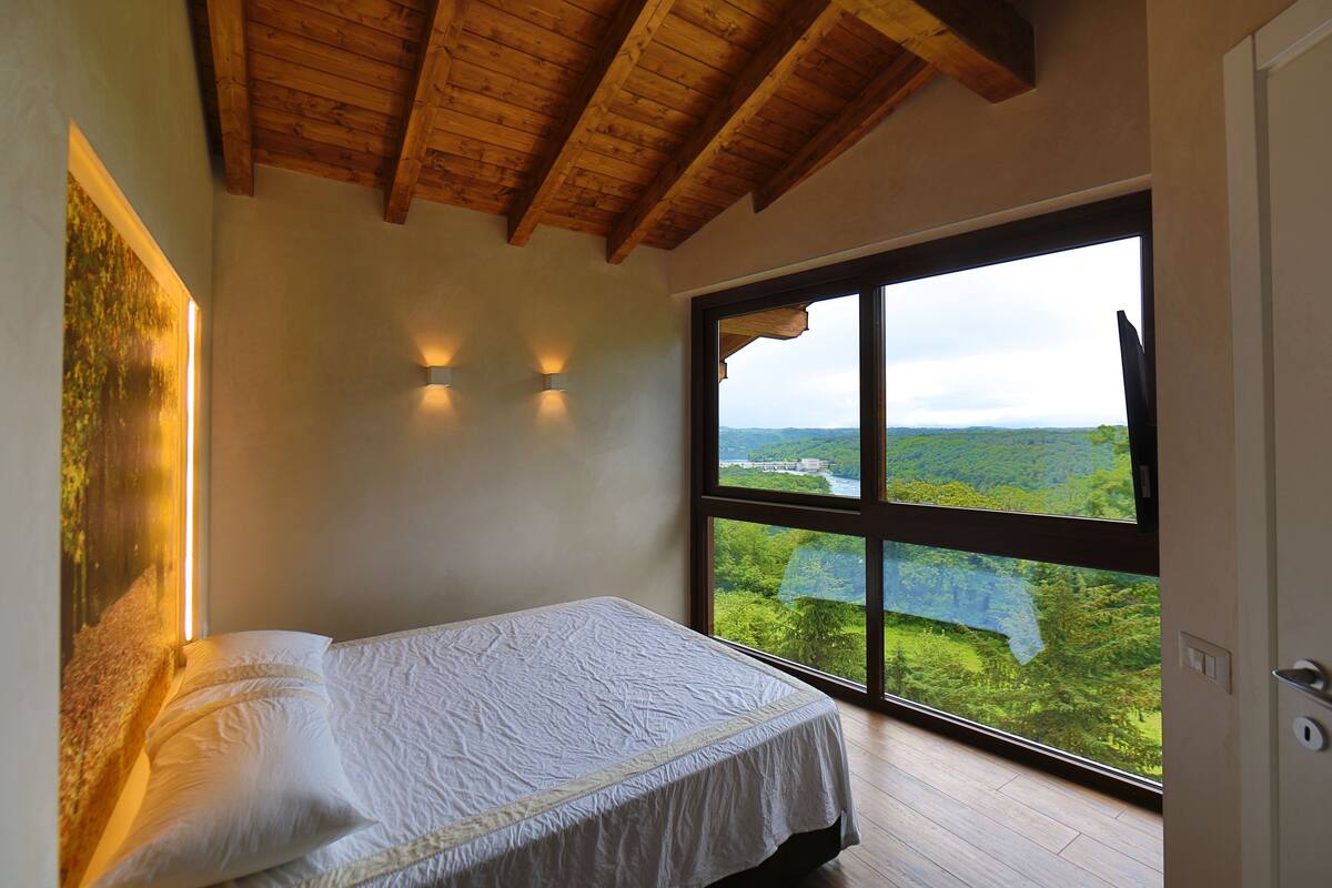 A bedroom with a large window, wooden ceiling beams, and a bed with white bedding.