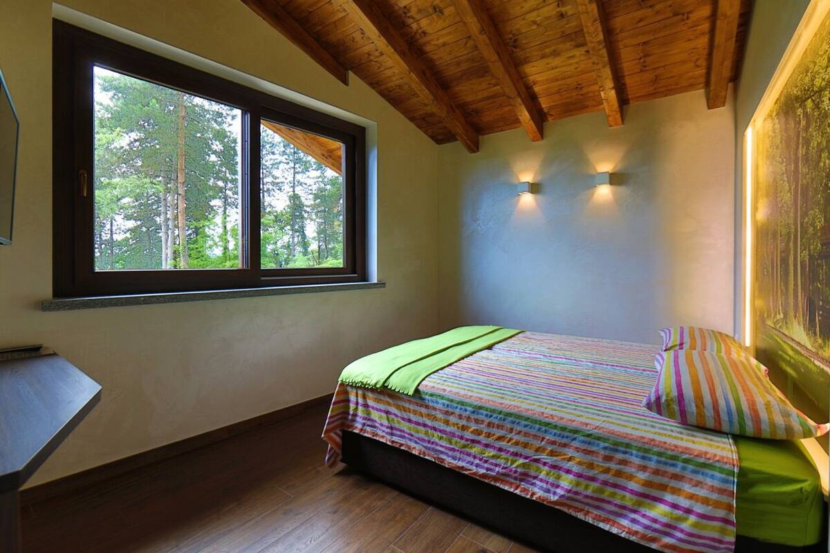 A bedroom with a large window, wooden ceiling beams, and a bed with striped bedding.