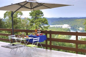 An outdoor dining area with a table and chairs, a table umbrella, and a scenic view of a river and bridge.