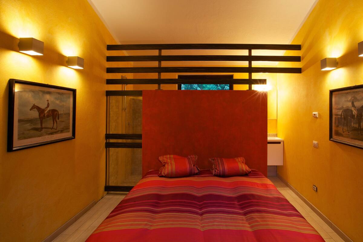 A hotel room with a bed, two framed pictures, a window, and a red curtain.