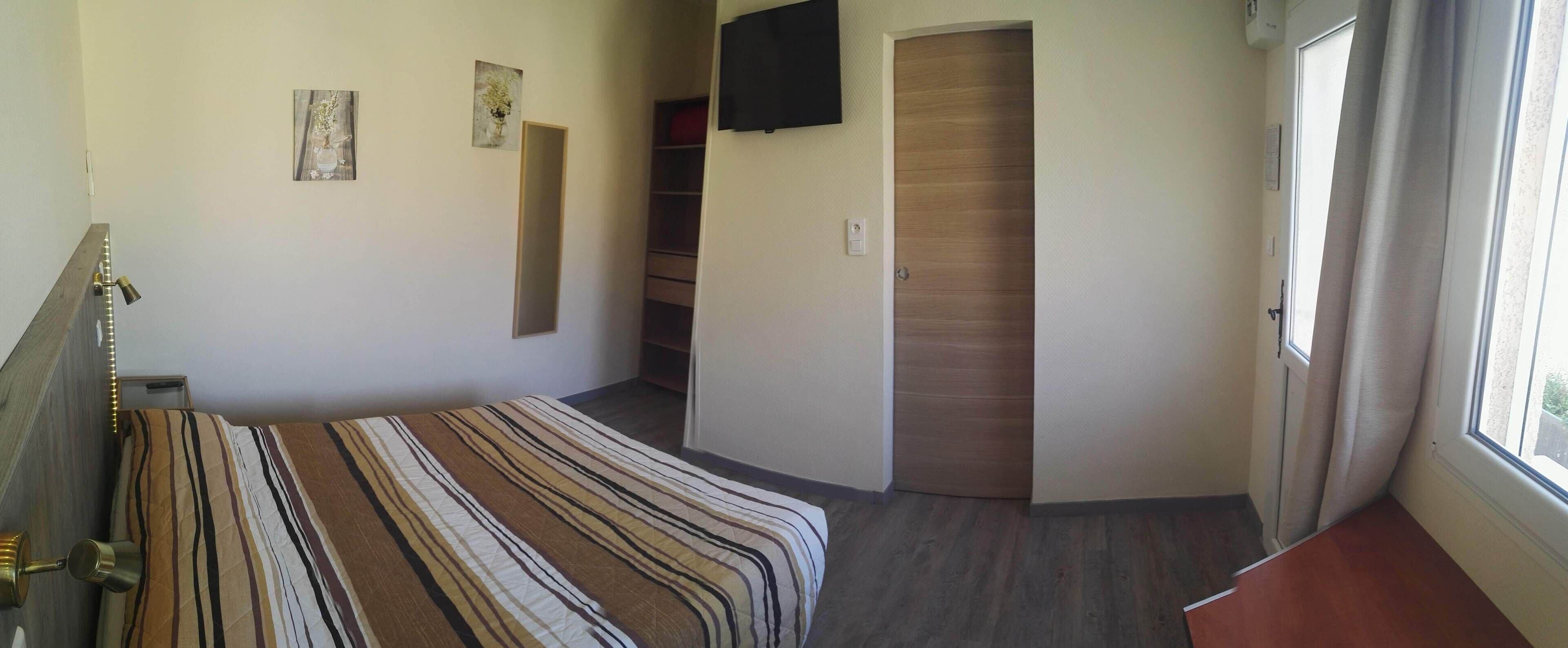 Un dormitorio con cama, televisión, puerta y ventana.