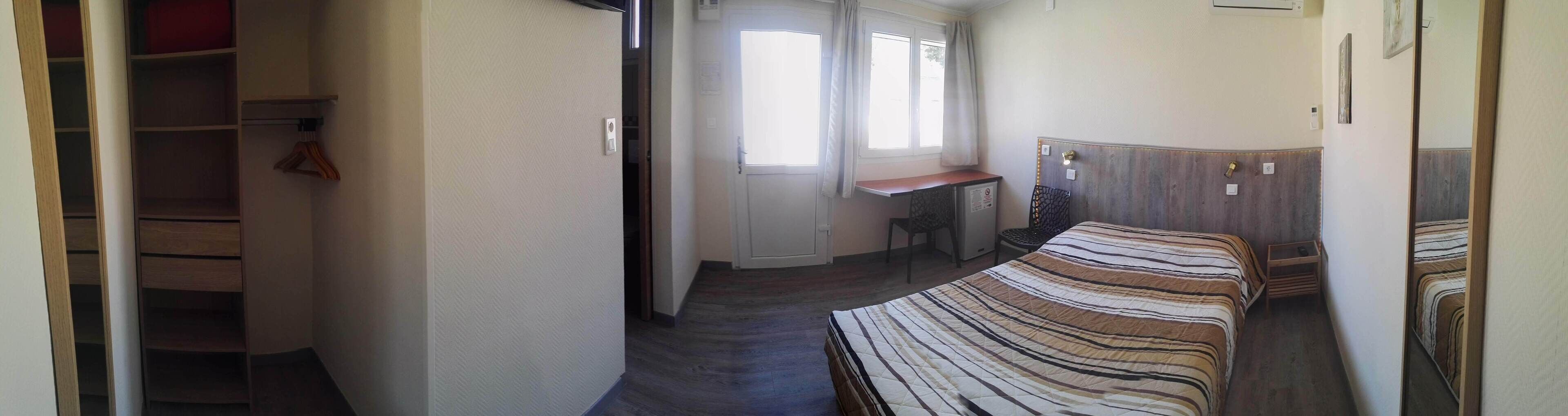 A narrow hallway leading to a bedroom with a bed, a desk, and a chair.