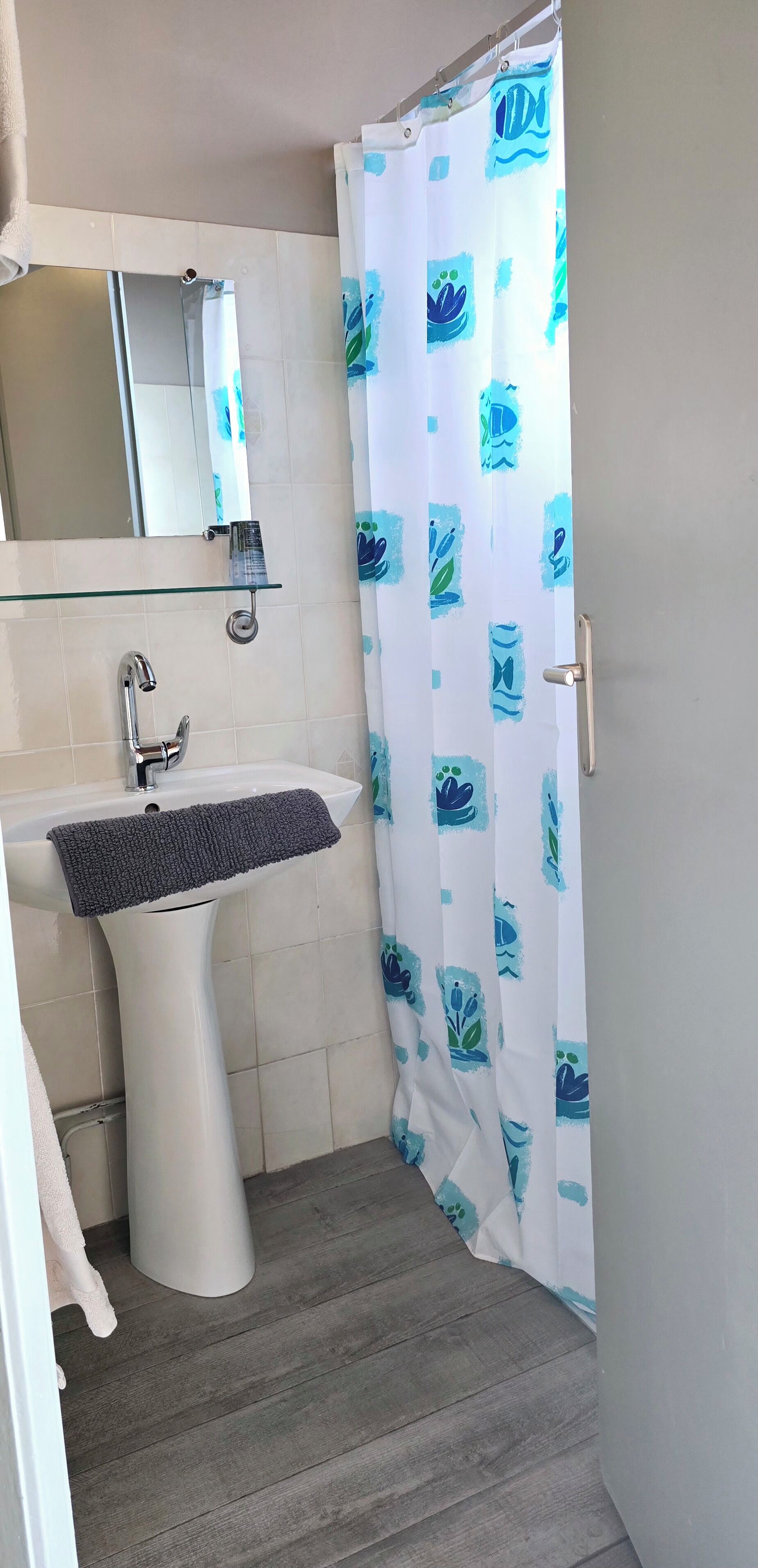 Un baño con lavamanos blanco, espejo y cortina de ducha con diseño azul.