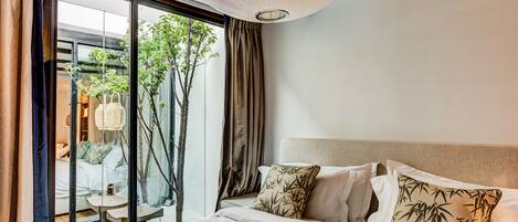 A hotel room with a large bed, a view of a garden through a sliding glass door, and a ceiling light fixture.