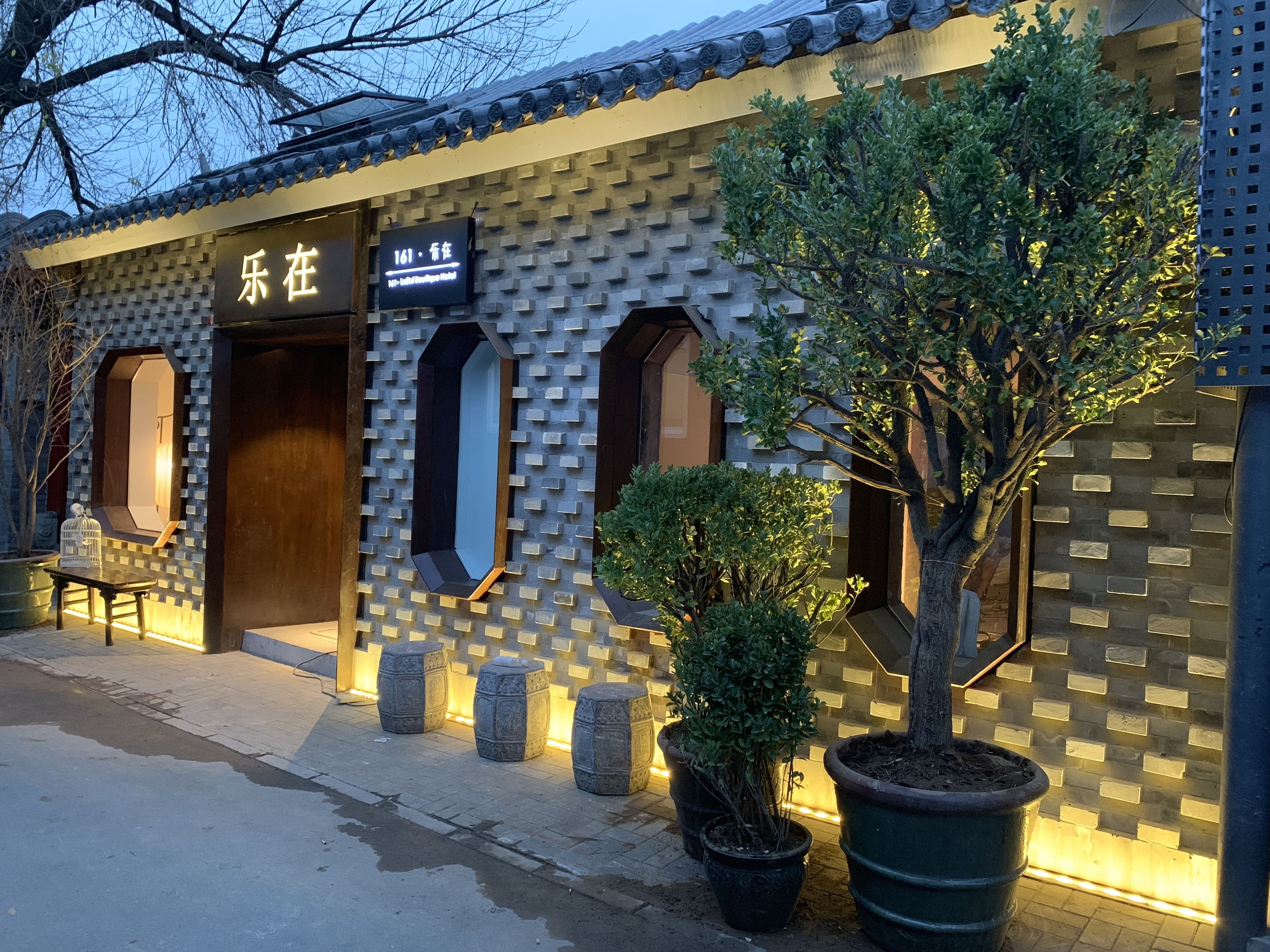 Un hotel con fachada tradicional, que muestra un letrero con el nombre y número. Hay plantas en macetas y un banco afuera.