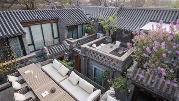 A traditional courtyard with tiled roofs, a wooden deck with seating, and a blooming tree.