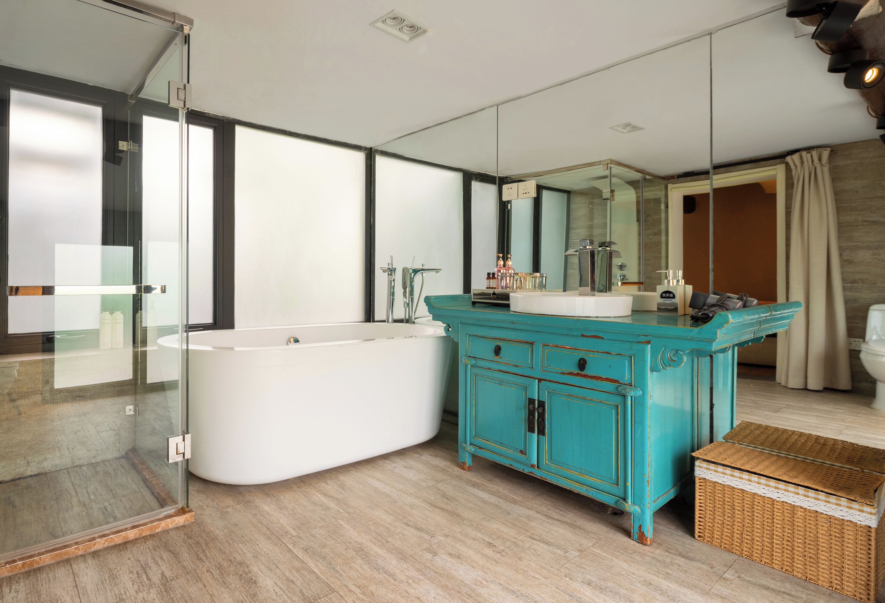 A modern bathroom with a freestanding bathtub, a large mirror, and a teal vanity.
