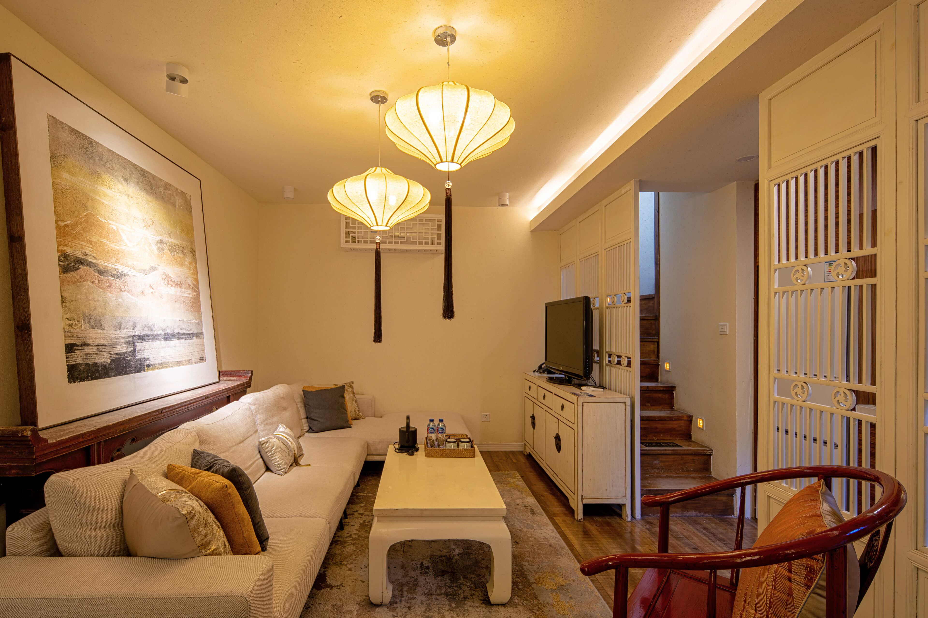 A living room with a sofa, coffee table, and a TV. There are two pendant lights hanging from the ceiling.