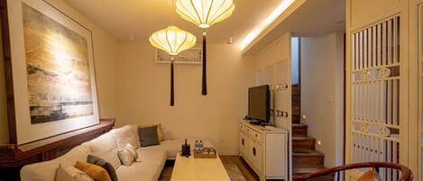 A living room with a sofa, coffee table, and a TV. There are two pendant lights hanging from the ceiling.