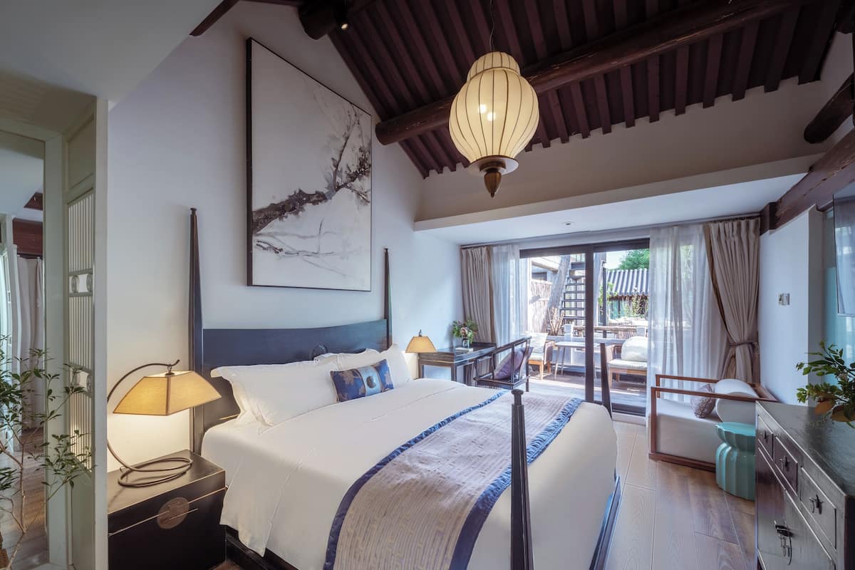A spacious bedroom with a large bed, a ceiling fan, a nightstand, a bedside table, and a view of the outdoor area.