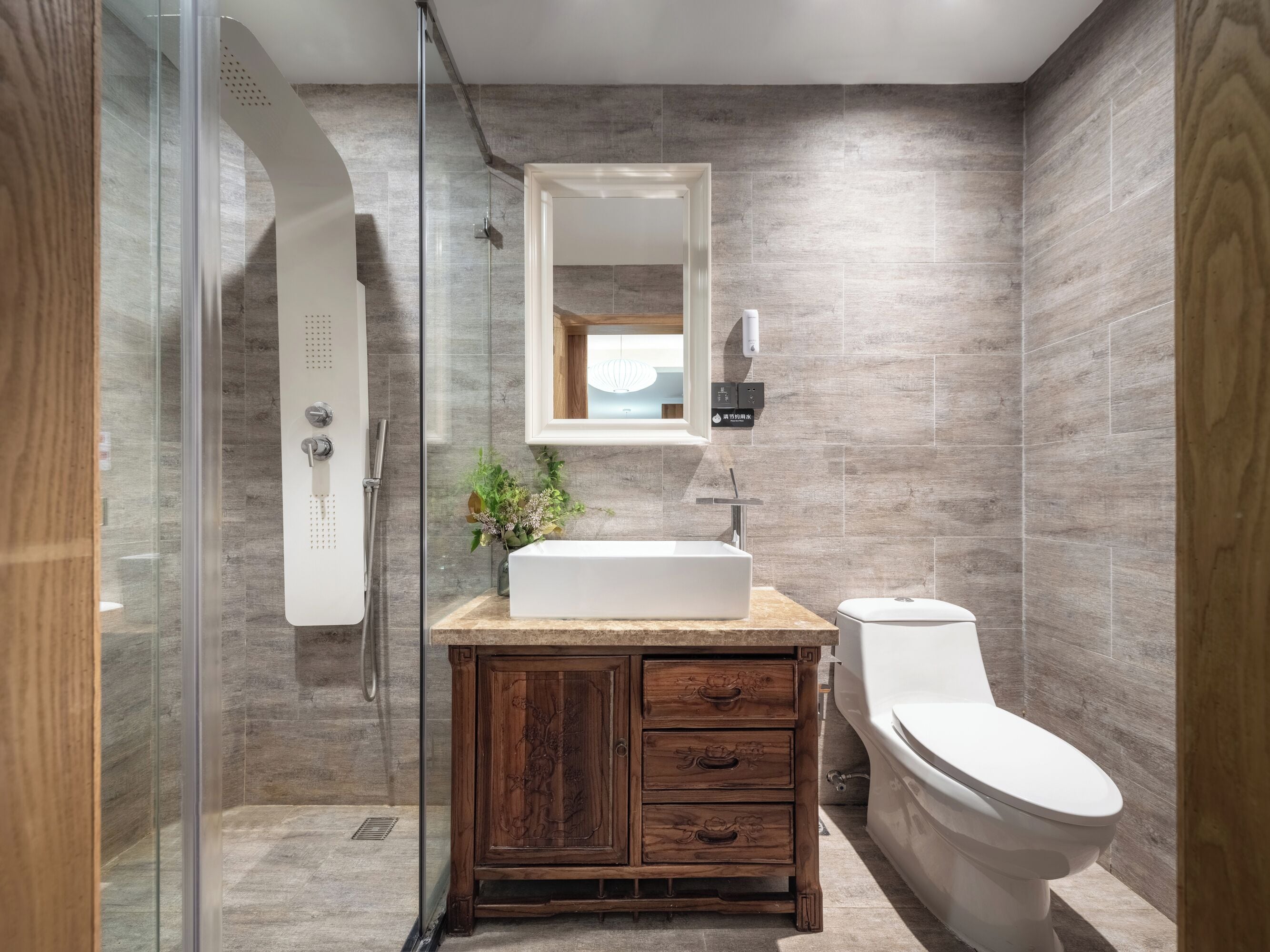 A modern bathroom with a glass-enclosed shower, a wooden vanity with drawers, a white sink, and a toilet.