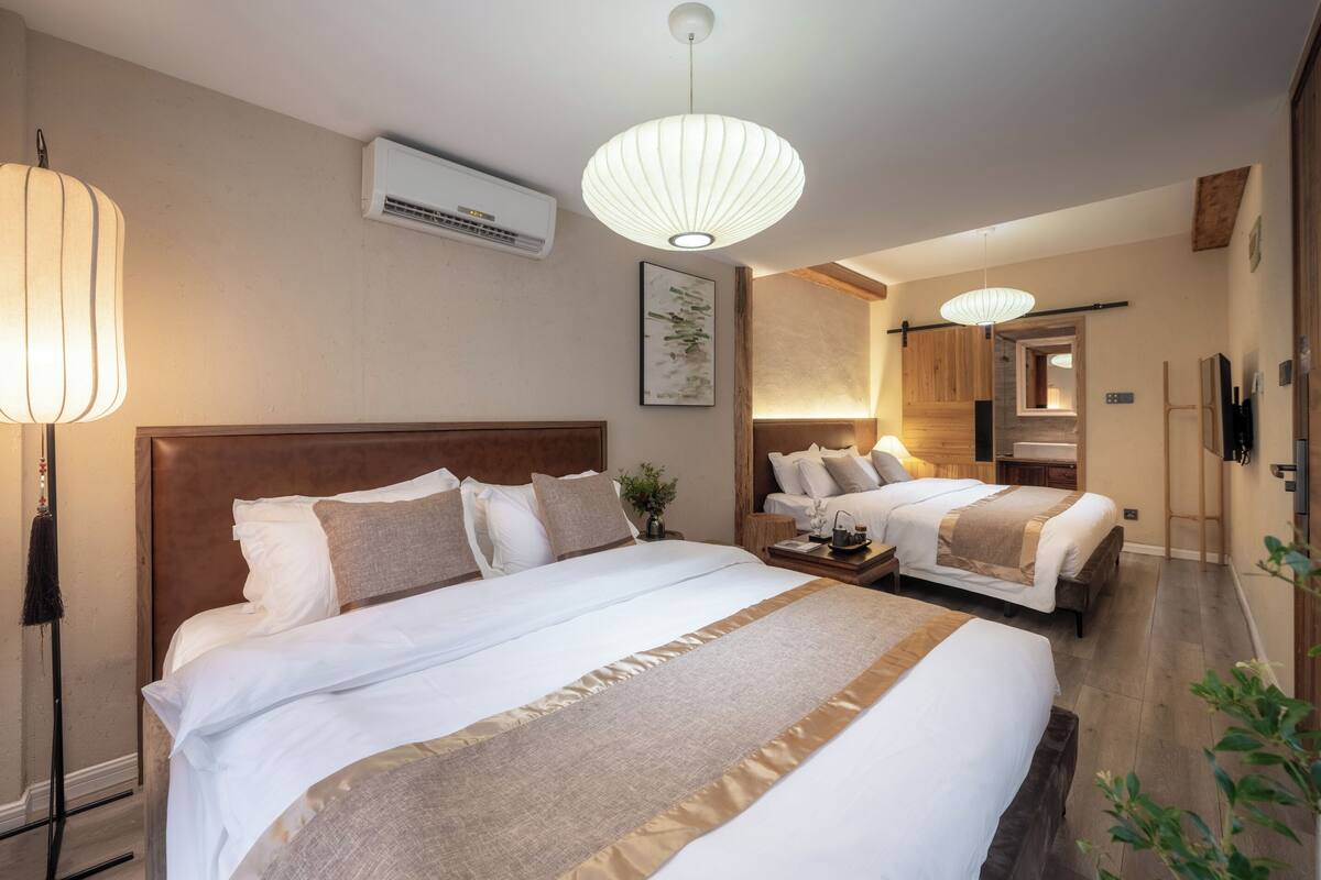A hotel room with two beds, a wooden headboard, a large window, and a ceiling fan.