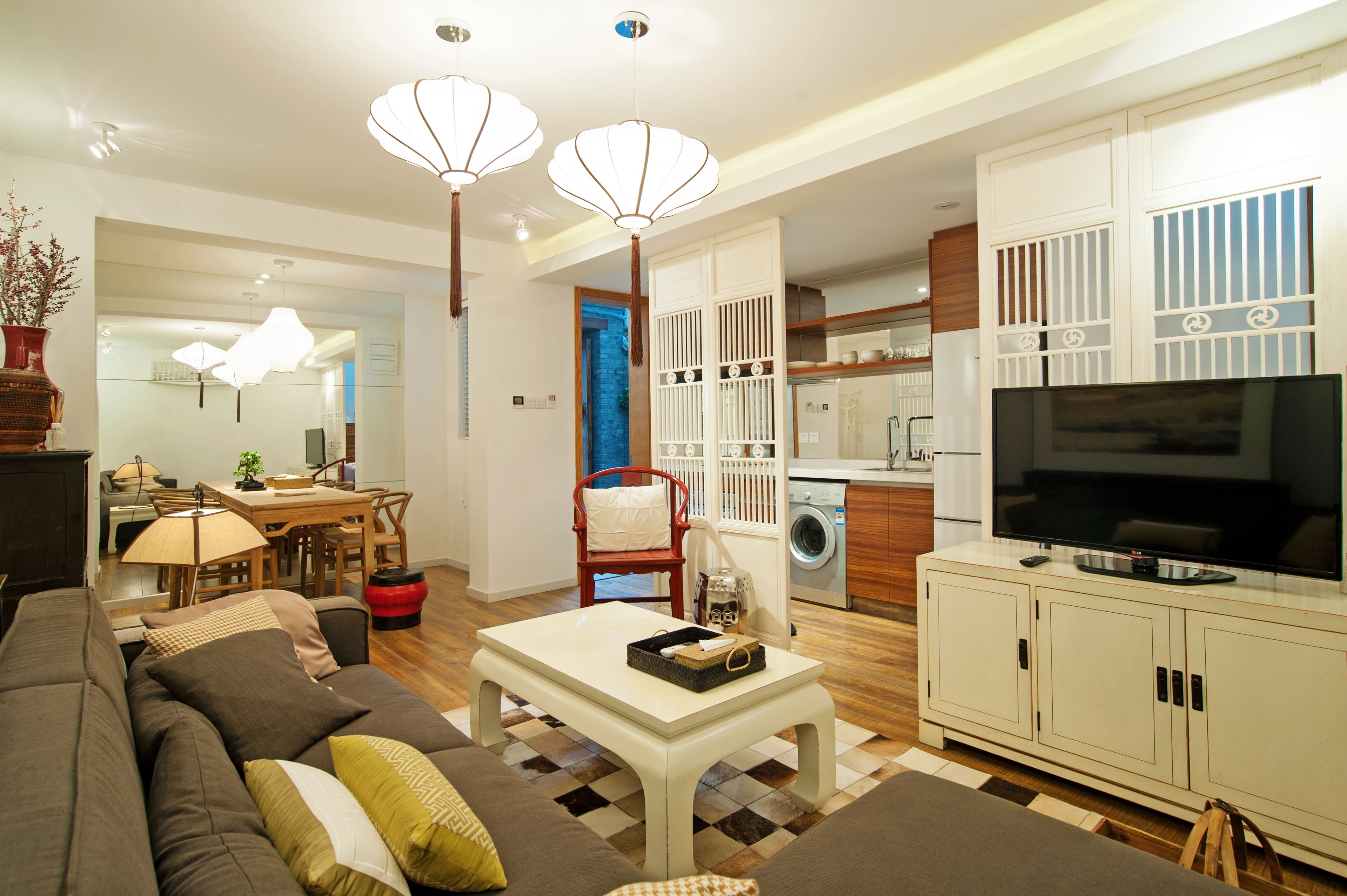 A modern living room with a sofa, coffee table, and TV. There is a kitchen area with a washing machine and a dining area with a table and chairs.