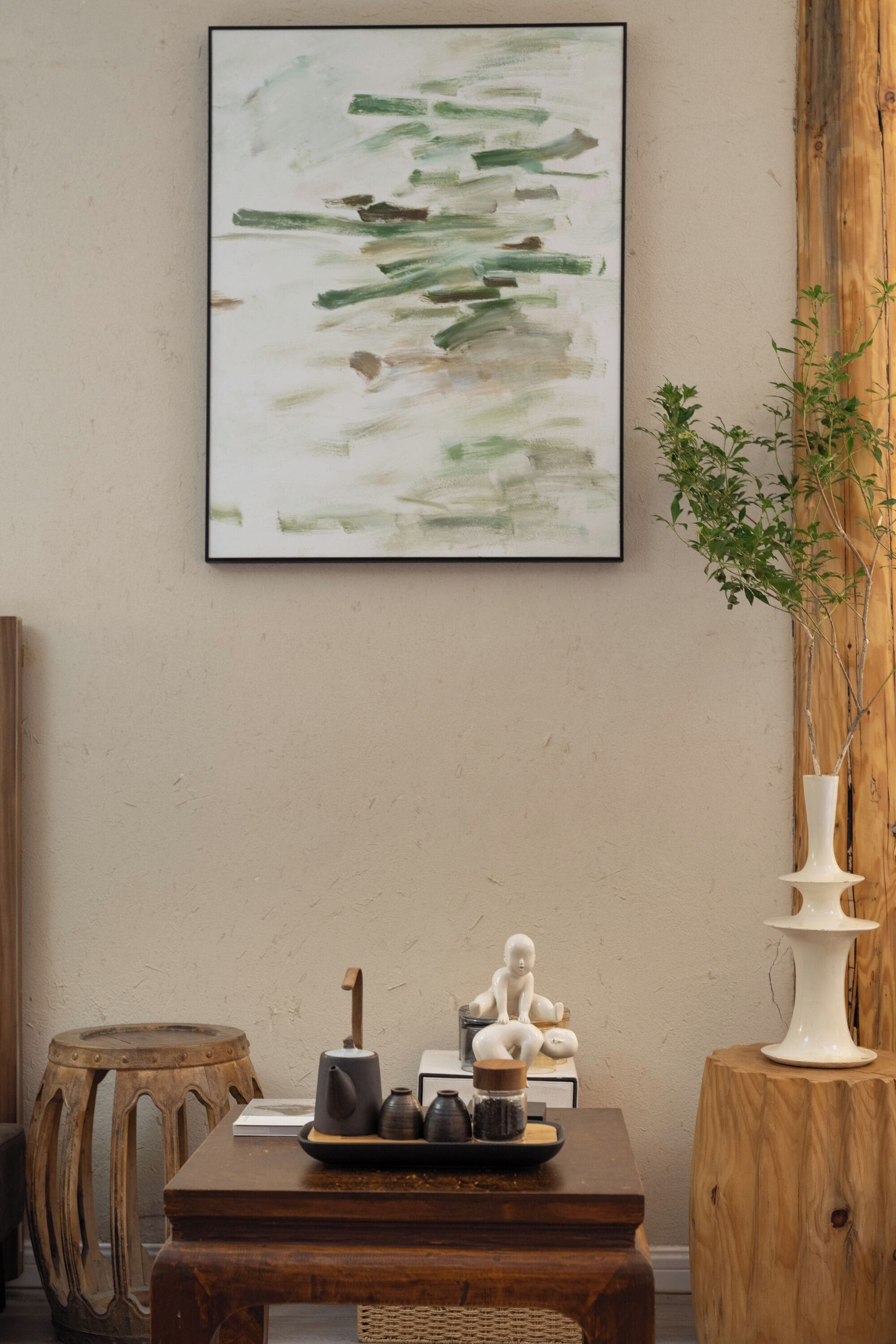 Une pièce avec une table en bois, un vase blanc et un tableau abstrait encadré accroché au mur.