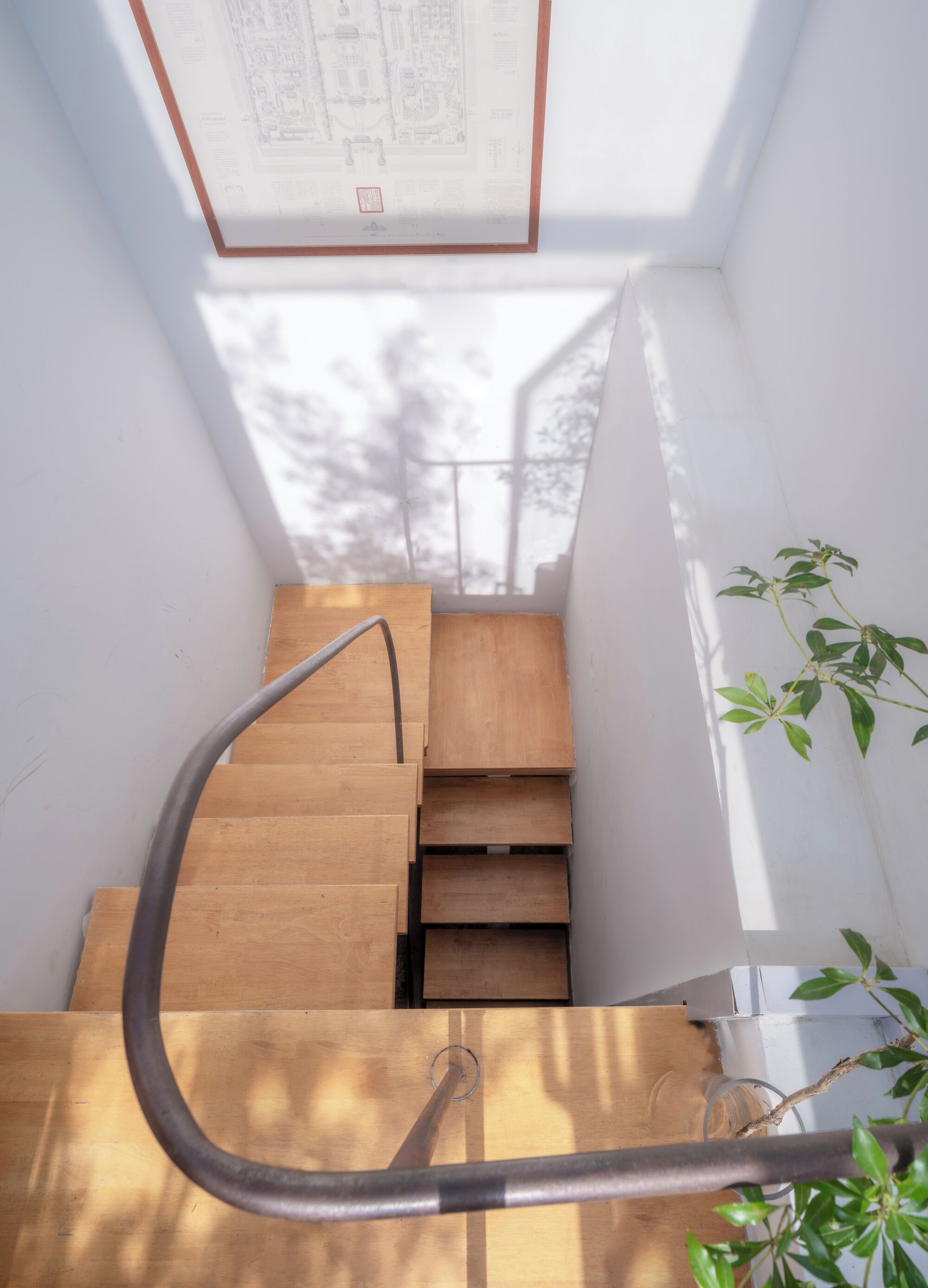 A wooden staircase with a metal handrail, leading to a landing with a framed architectural drawing.