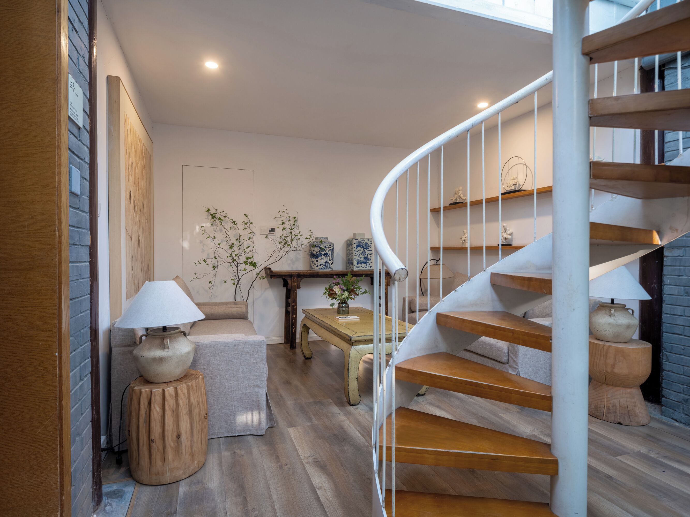 A modern interior with a spiral staircase, wooden flooring, and a cozy seating area with a lamp and a vase.