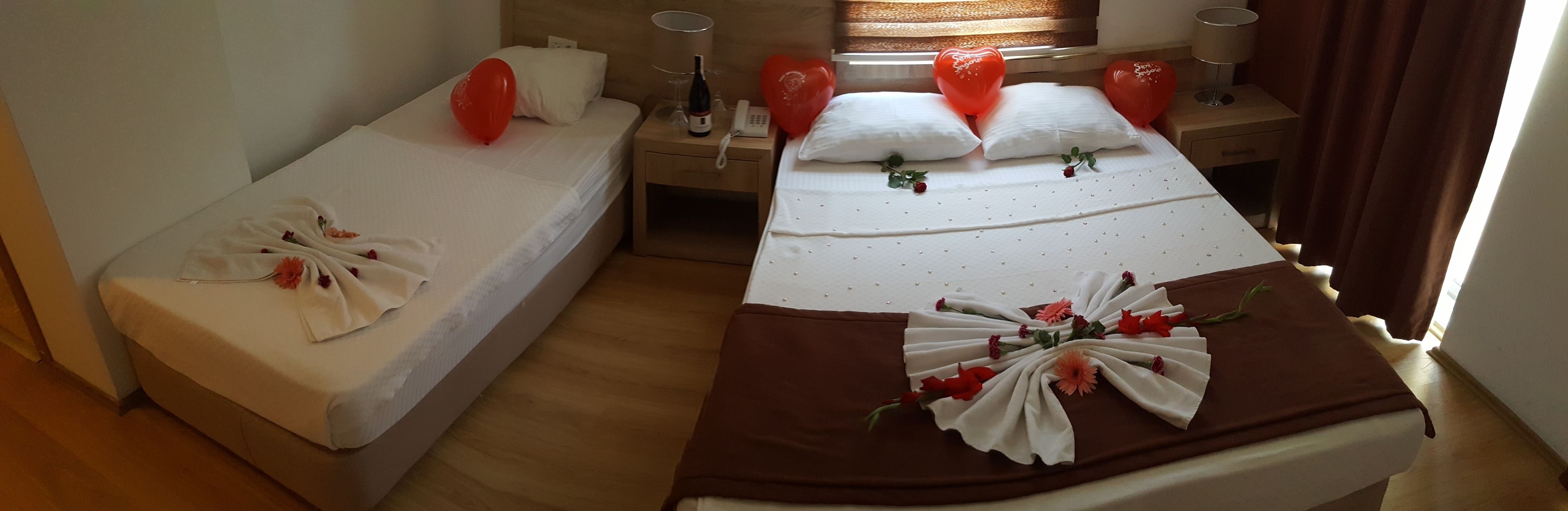 A hotel room with two beds, a wooden floor, a window with curtains, and a bedside table with a lamp and a bottle.