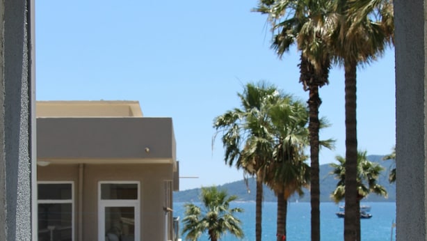 A balcony with a view of a beach, palm trees, and a building with a balcony. - The Marmaris Boutique Hotel (Marmaris)