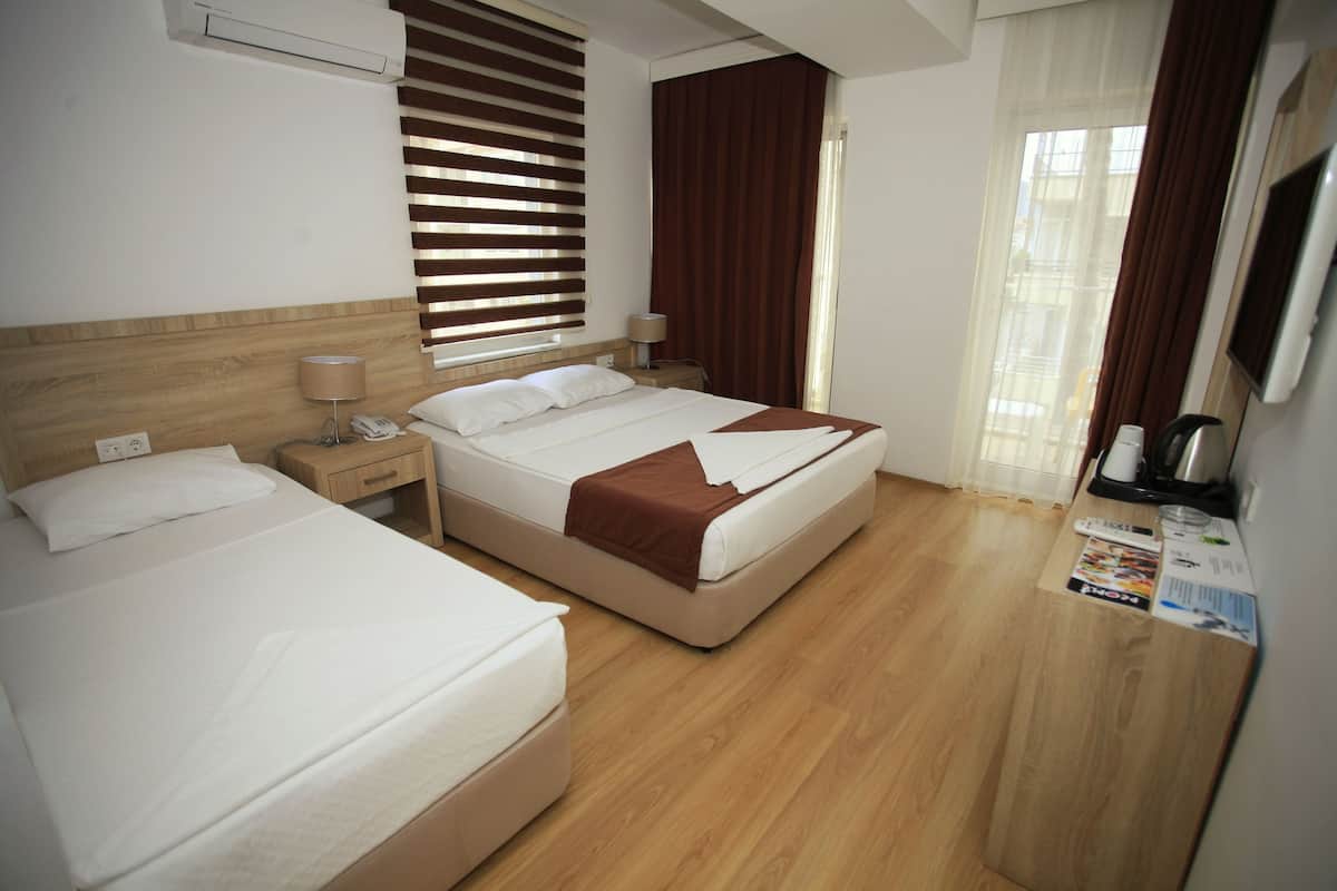Camera d'albergo con due letti, una testiera in legno, un comodino con una lampada, una televisione e una finestra con persiane.