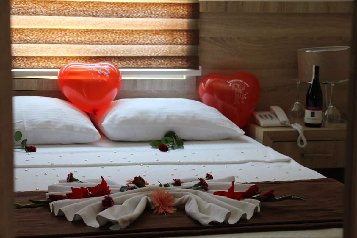 Un letto rifatto con cura, palloncini a forma di cuore, una bottiglia di vino e fiori sparsi.