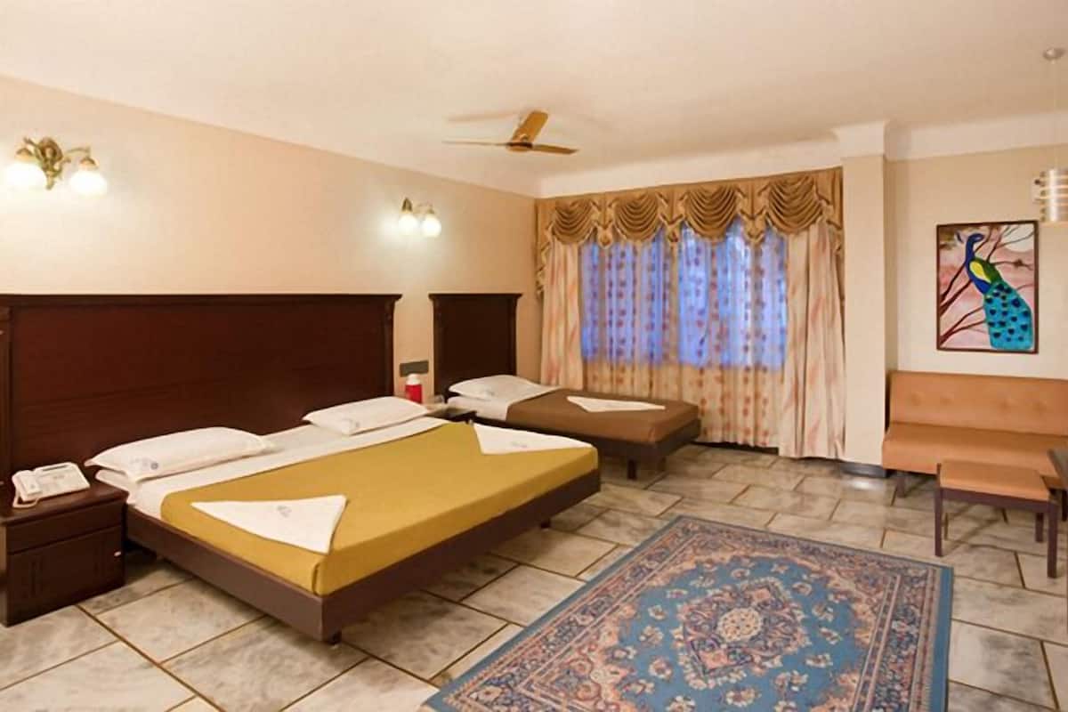 A hotel room with a large bed, a smaller bed, a desk, a chair, a nightstand, a telephone, a ceiling fan, and a window with curtains.
