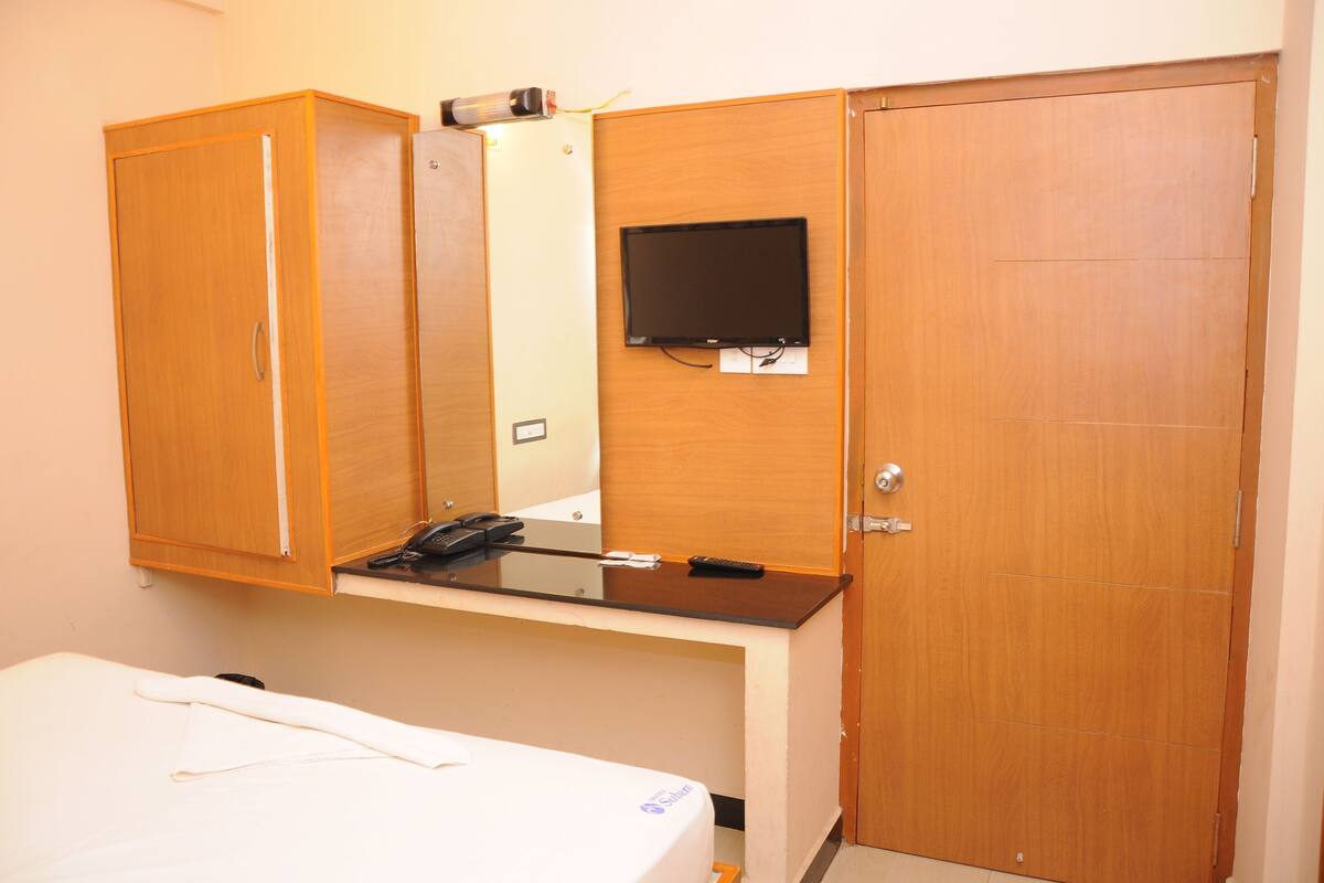 A hotel room with a bed, a desk with a flat-screen TV, and wooden wardrobes.