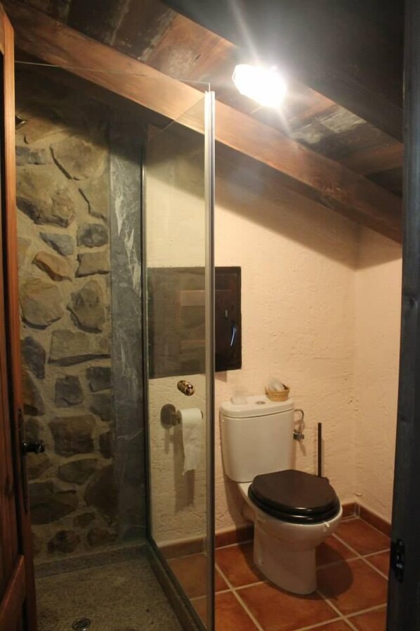 Ein Badezimmer mit Duschkabine aus Stein, Toilette und Fliesenboden.