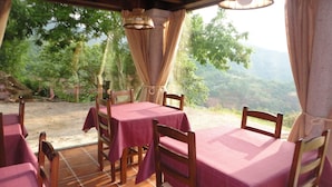 A dining area with tables covered in red tablecloths, wooden chairs, and a view of a forested hillside. - Casería La Infiesta (Caso)