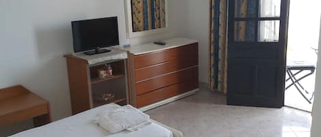 A bedroom with two beds, a TV, a dresser, and a window with curtains.