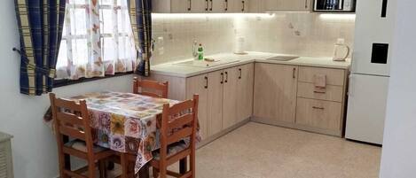 A compact kitchen with a dining table, wooden cabinets, a microwave, and a refrigerator.