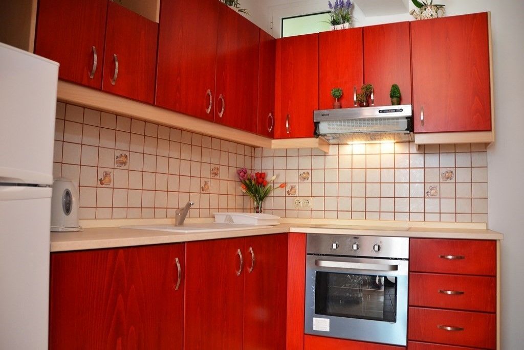 A kitchen with red cabinets, a stainless steel oven, and a tiled backsplash.