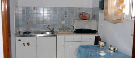 Una cocina compacta con lavamanos, estufa y una pequeña mesa con mantel.