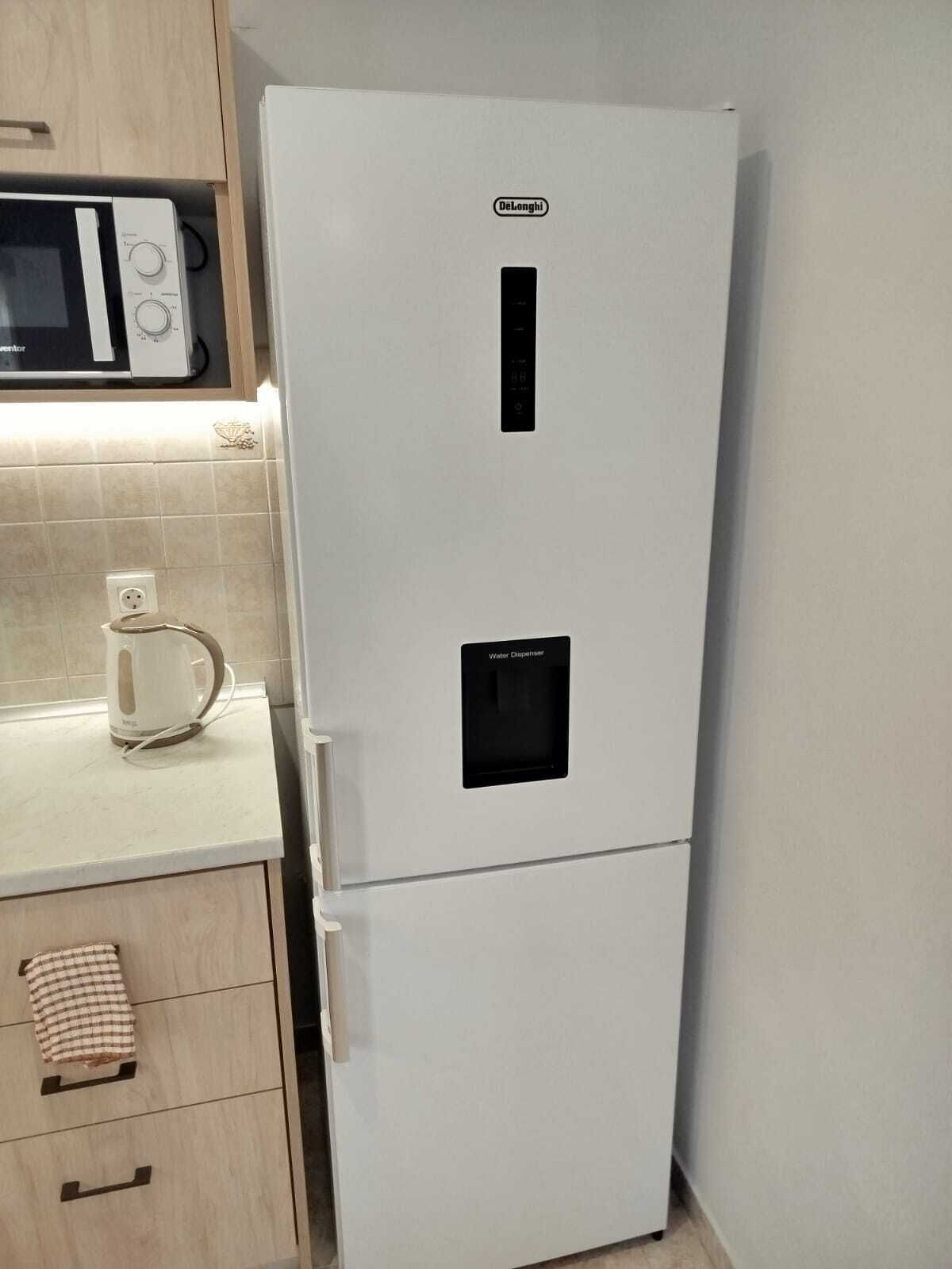 Et hvidt køleskab med vanddispenser og en mikrobølgeovn ovenpå.