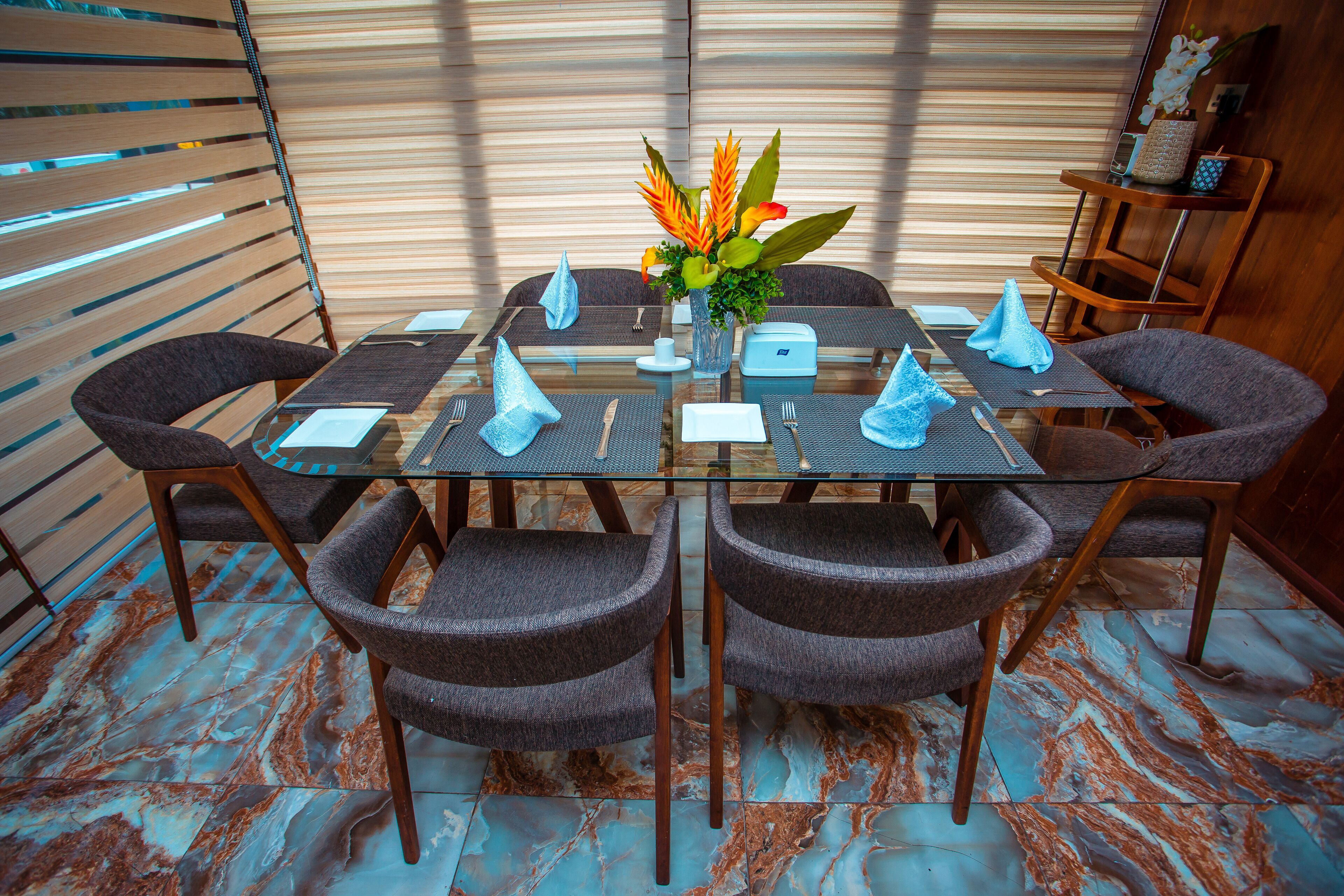 A dining area with a glass table, six chairs, and a vase of flowers.