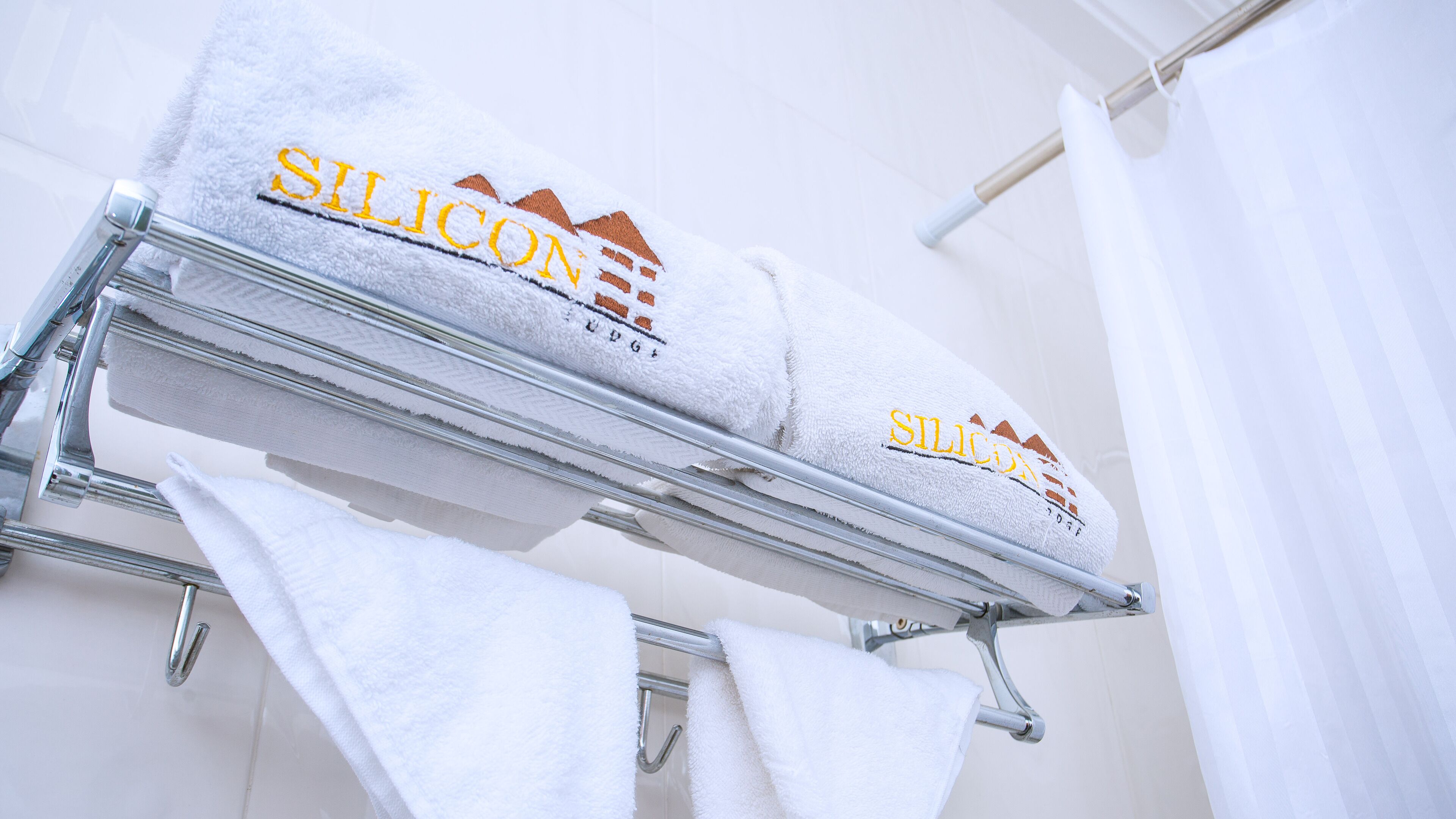 Two white towels with 'Silicon' branding on a metal rack in a bathroom.
