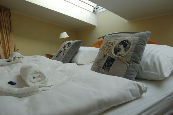 Una cama bien hecha con sábanas blancas, una toalla enrollada y almohadas decorativas con diseños antiguos.