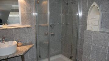 A bathroom with a granite-tiled shower enclosure, a sink with a mirror, and a small decorative alcove with a shelf.